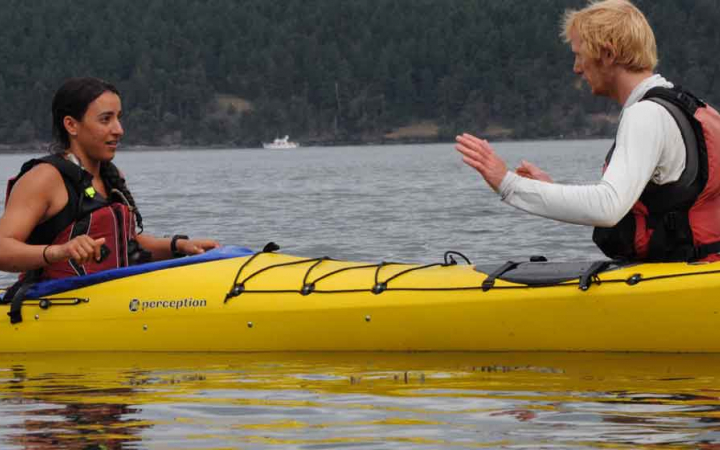 an outward bound instructor gives direction to a student in a kayak